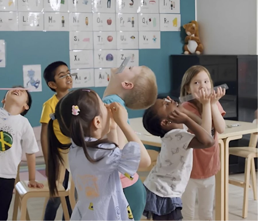 Children in a classroom laughing and looking up with joy, with alphabet cards visible on the wall behind them.